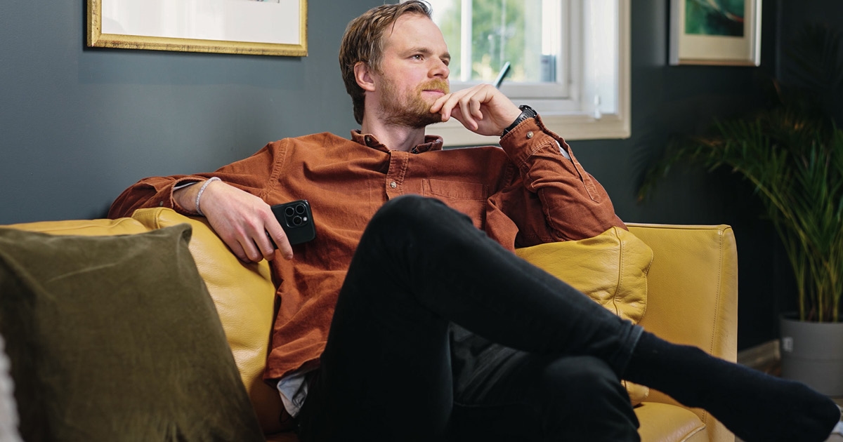 Mann som sitter i en gul sofa og ser tenkende ut i luften. Foto.