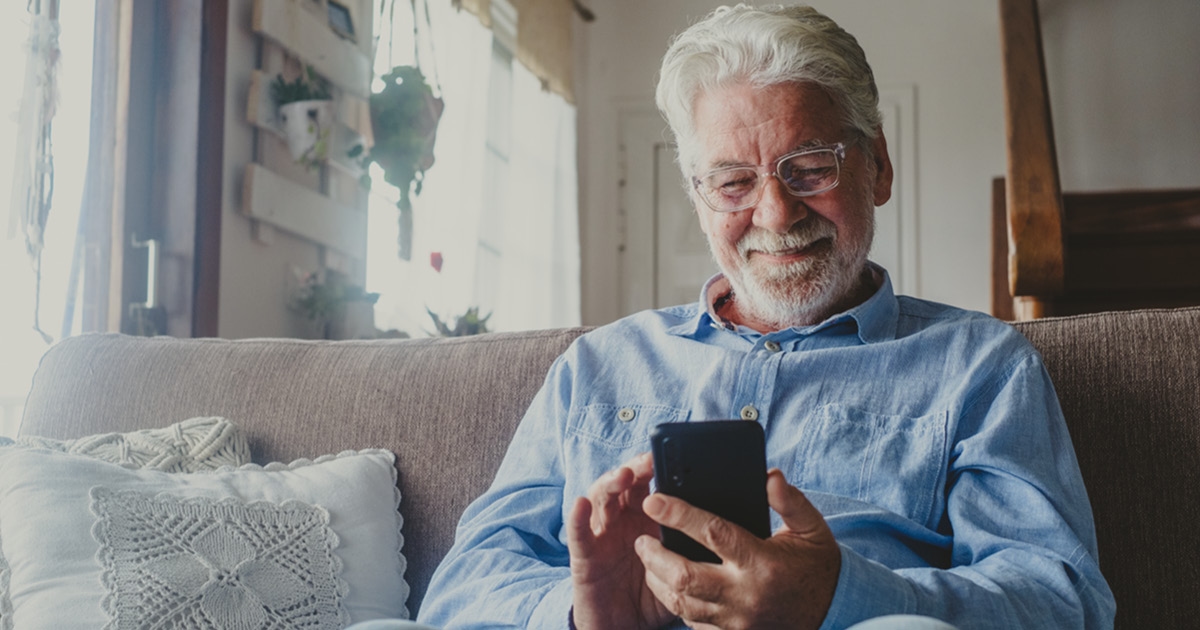 En gammel mann sitter og ser på mobilen sin. Foto.