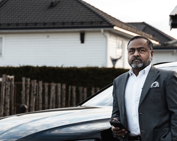Mann i dress foran bilen sin. Foto.