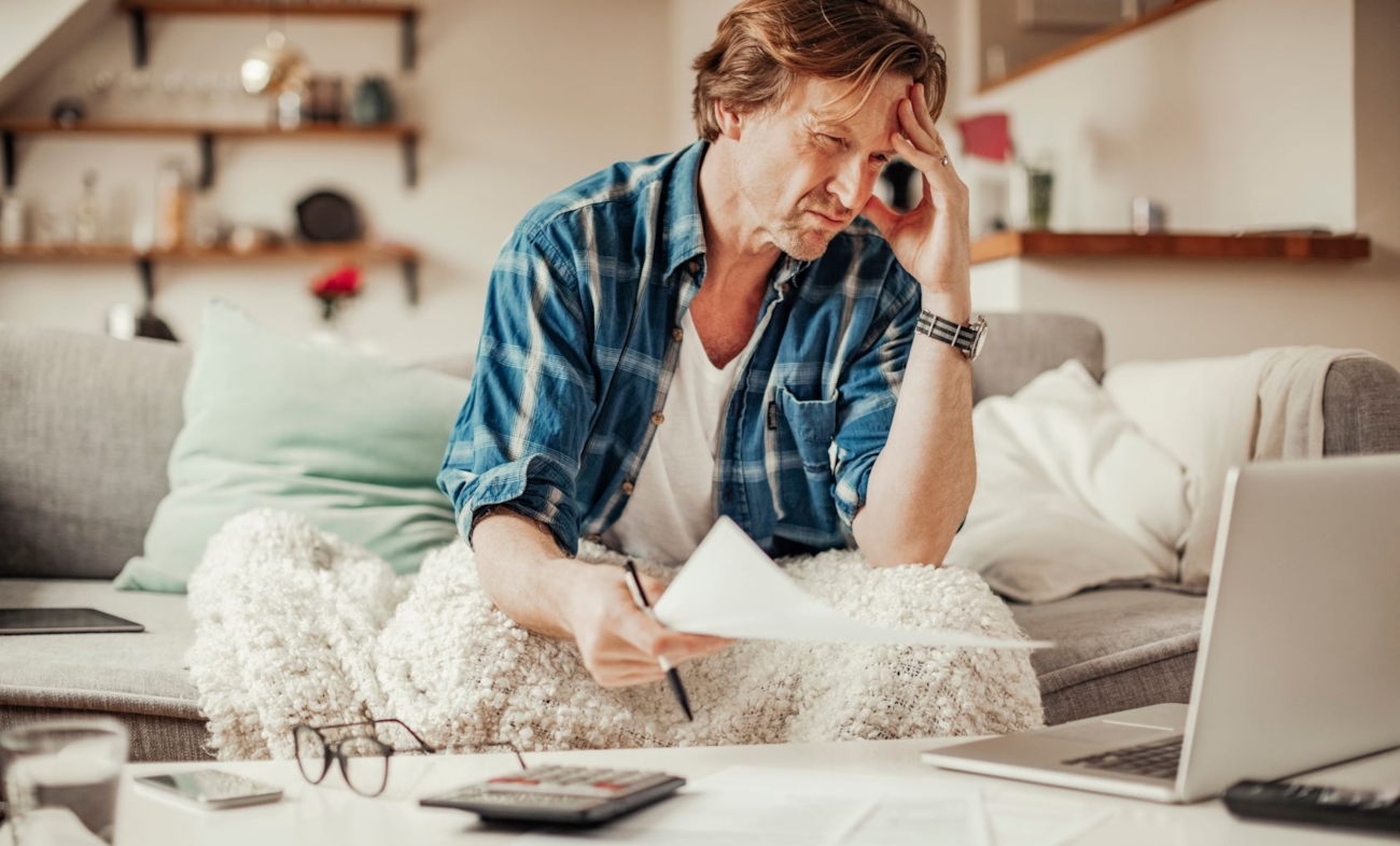 En fortvilet person som sitter og ser på et notat med telefonen liggende på bordet foran seg. Illustrasjonsfoto.
